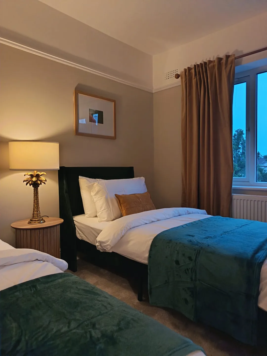 Twin bedroom with teal throws, gold-toned table lamp and warm beige curtains