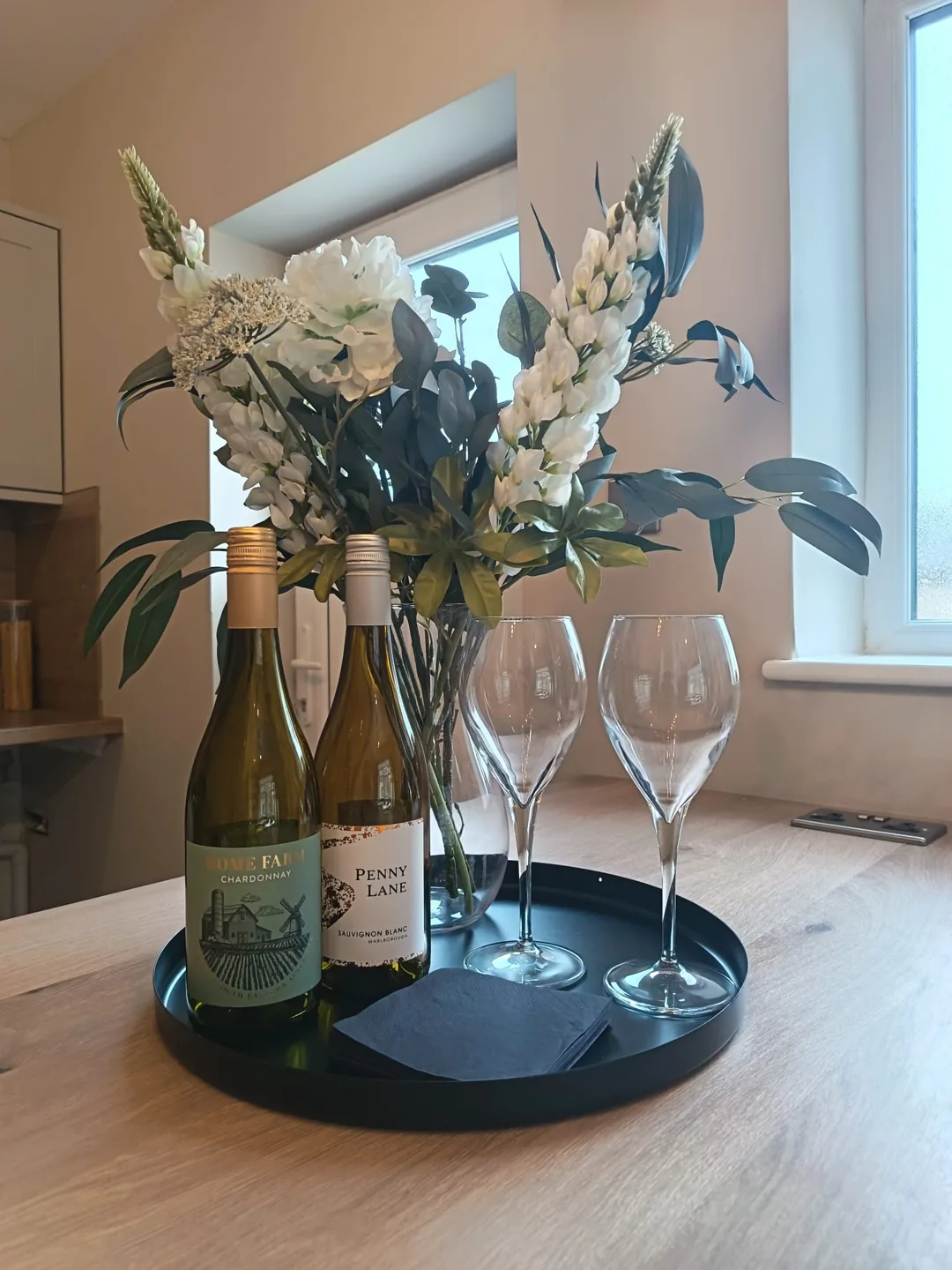 Welcome arrangement with flowers, glassware and bottles on a wooden counter
